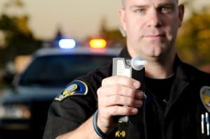 A police officer holding a breath test machine with his police car in the background. *the officer was blurred on purpose.